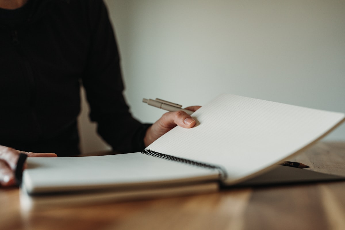 Hands hold a pen beside an open notebook.
